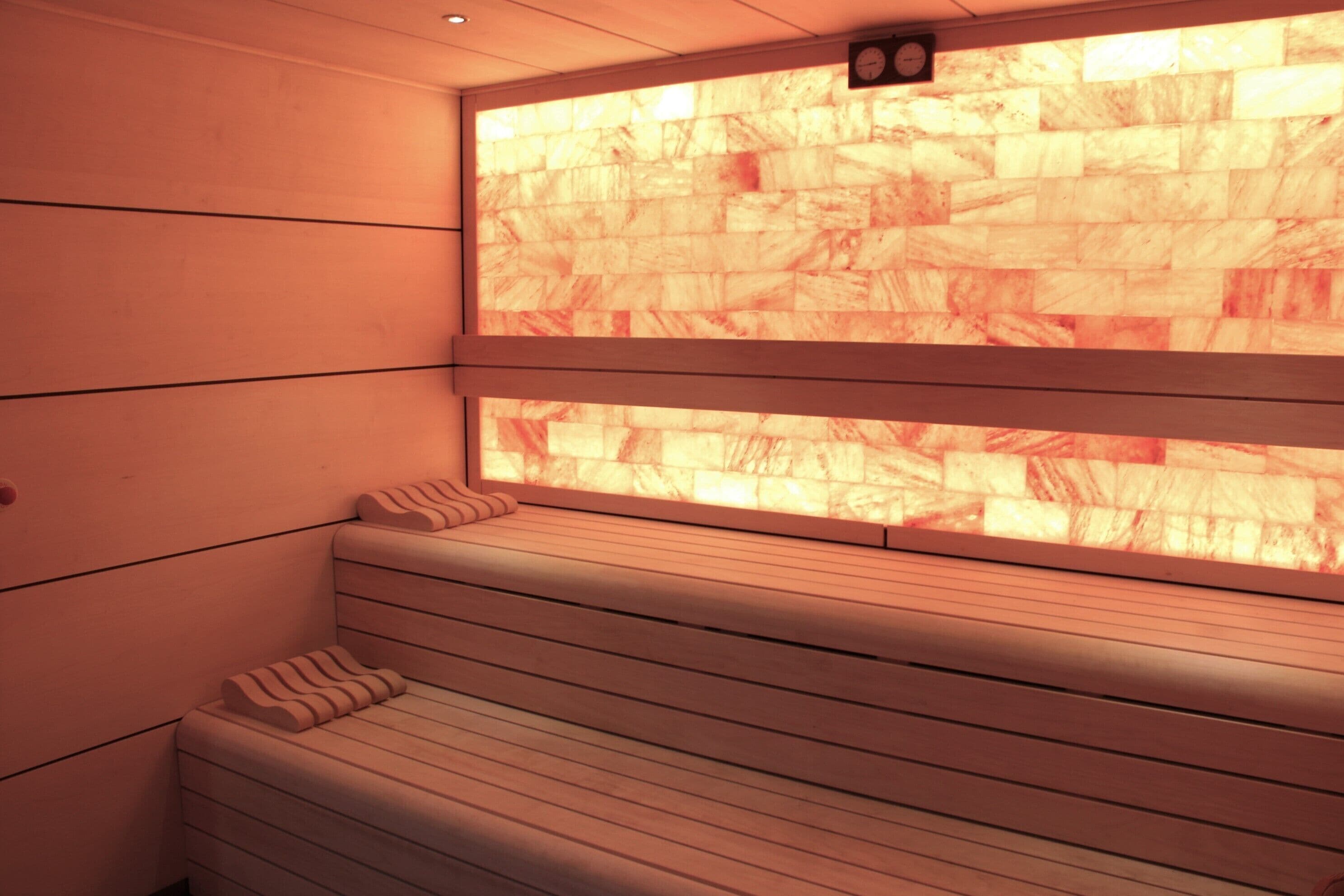 A sauna room with a wooden bench and a large window with a stone-like pattern.