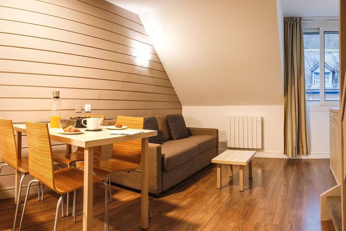 A modern, compact living space with a dining area, sofa, and staircase.