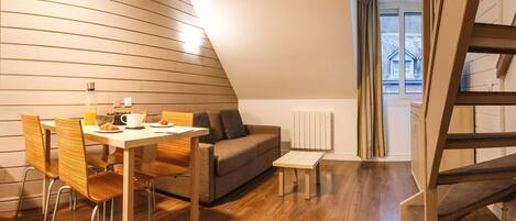 A modern, compact living space with a dining area, sofa, and staircase.
