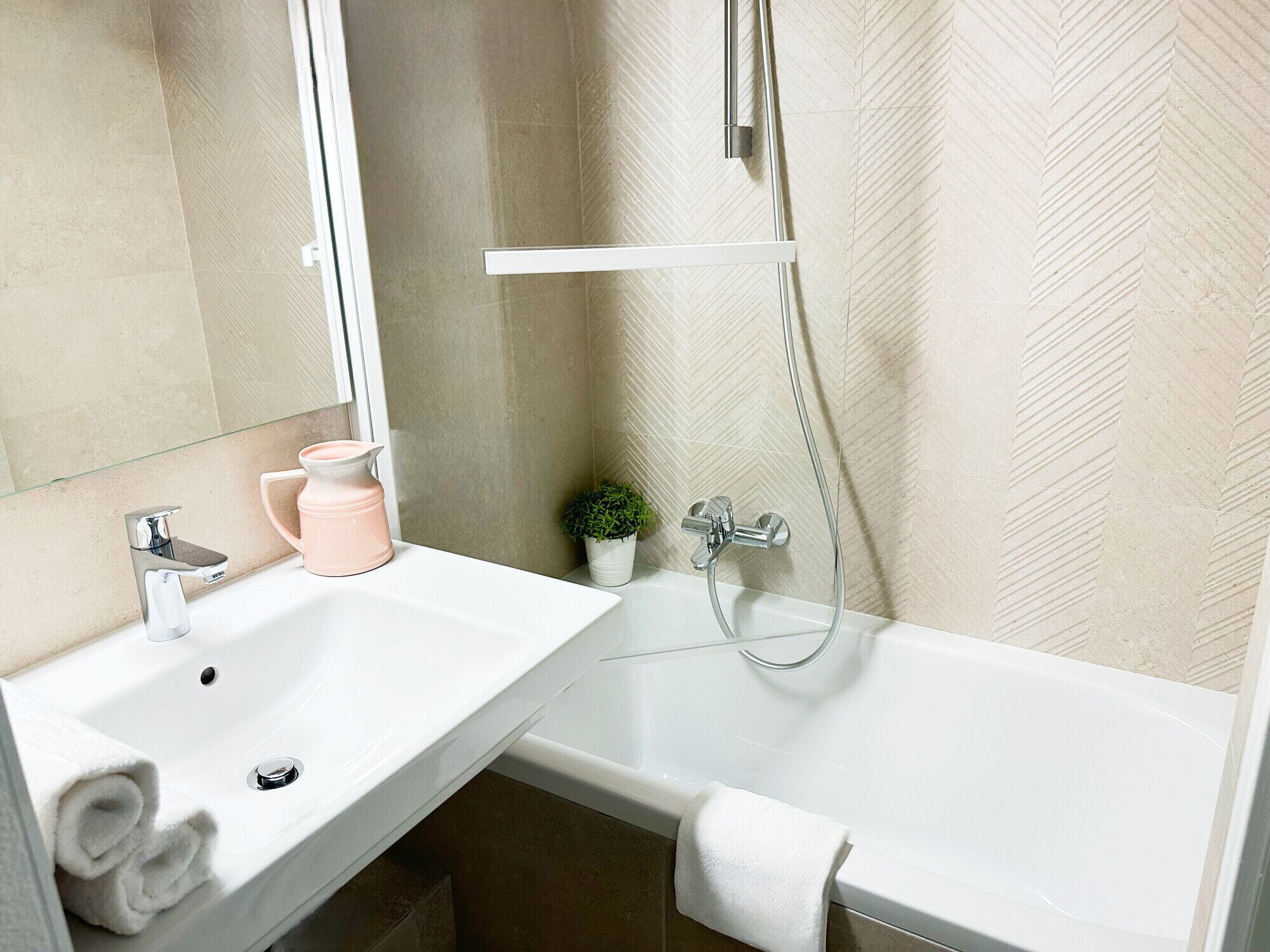 Un bagno moderno con un lavandino bianco, uno specchio, una doccia e una piccola pianta in vaso.