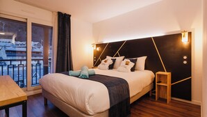 Una habitación de hotel moderna con una cama grande, una mesita de noche pequeña, vistas de la ciudad a través de un ventanal amplio y un balcón.