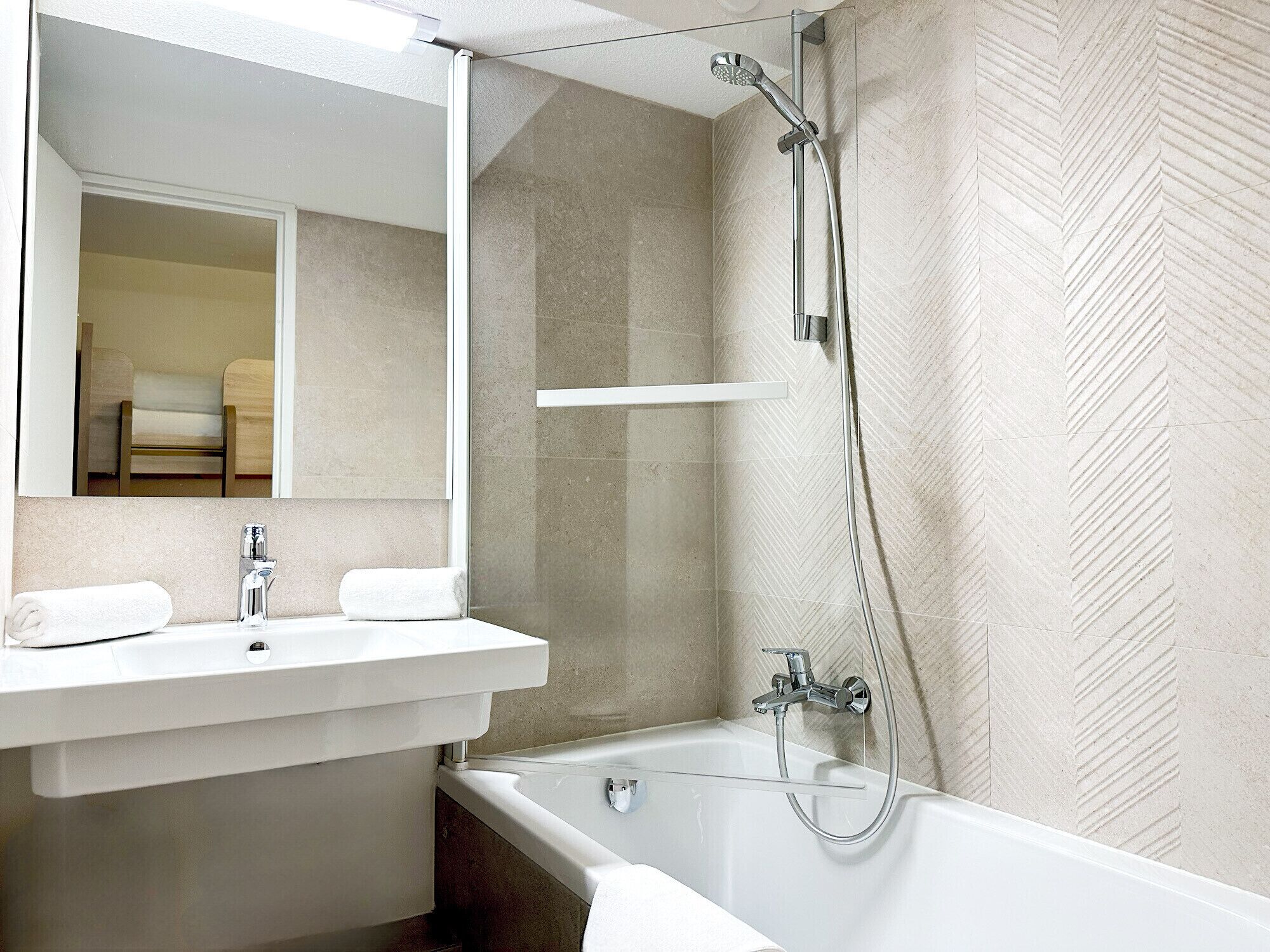 Un baño moderno con lavamanos, espejo y bañera blancos.