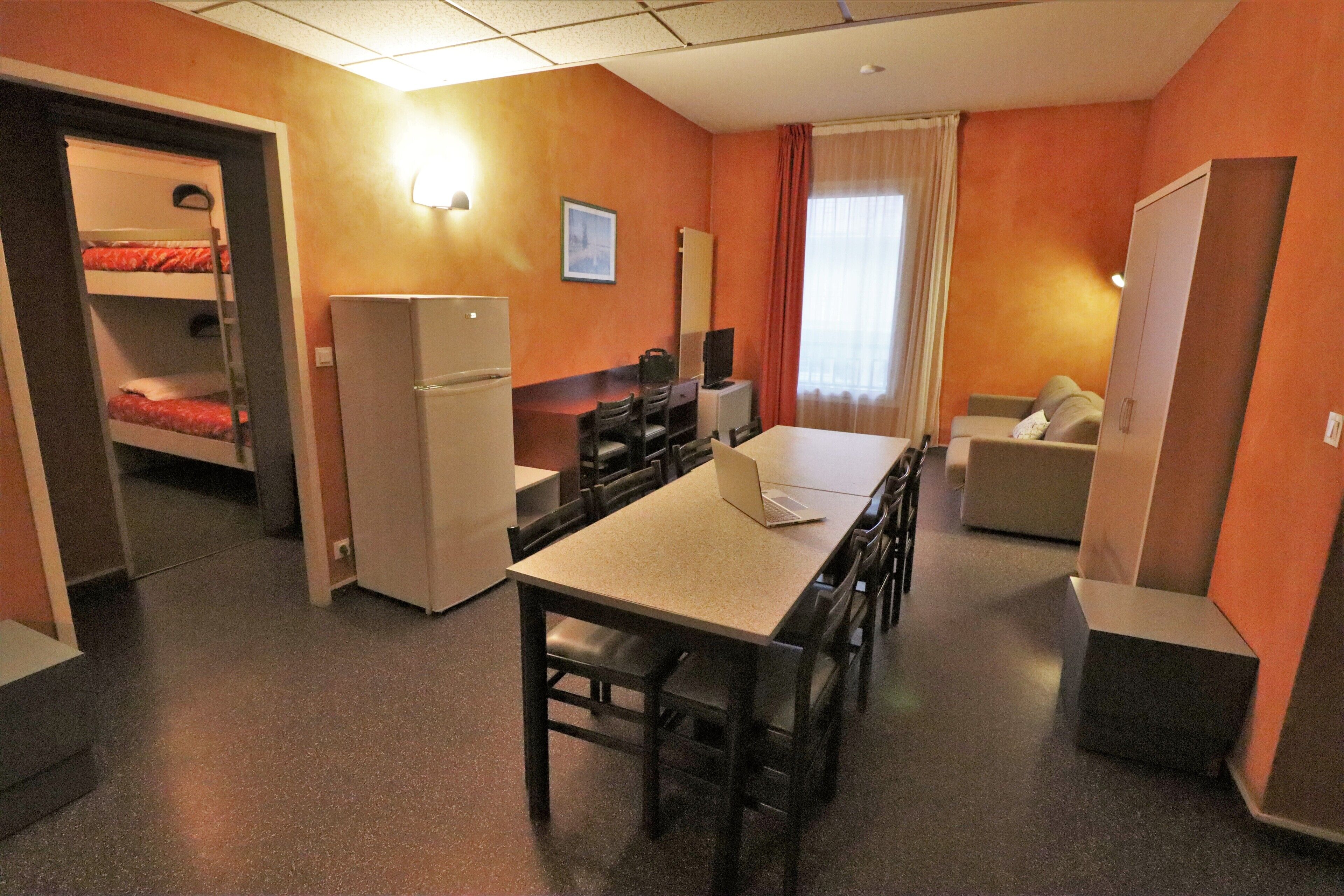 Ein kompaktes Hotelzimmer mit Etagenbetten, einer Küchenzeile, einem Essbereich und einer Sitzecke.