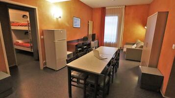 Ein kompaktes Hotelzimmer mit Etagenbetten, einer Küchenzeile, einem Essbereich und einer Sitzecke.