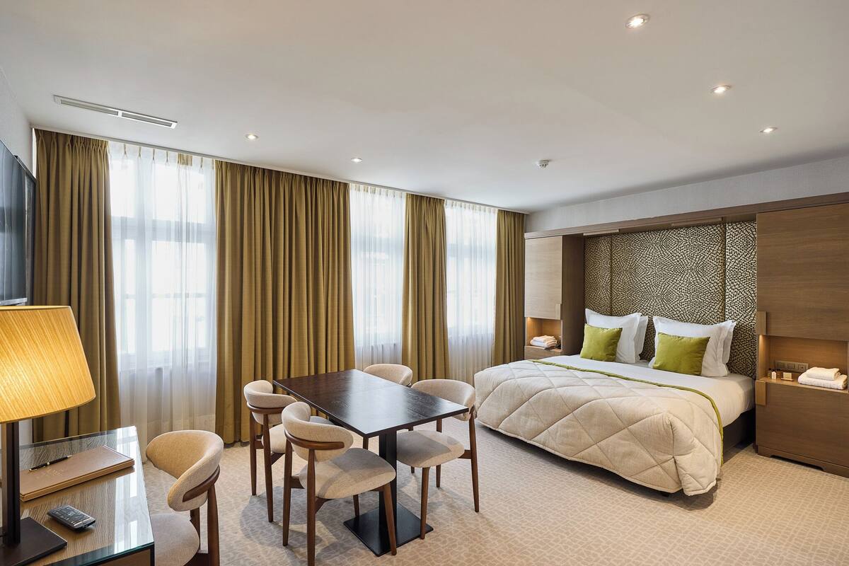 A hotel room with a bed, a desk with a lamp, and a chair.