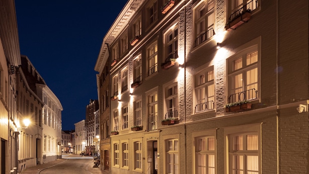 A cobblestone street lined with historic buildings, featuring balconies with potted plants and illuminated windows. - Aragon House (Bruges)
