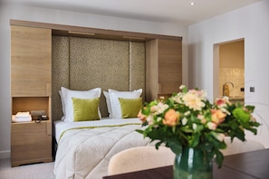 Quarto de hotel moderno com cama grande, mesa de cabeceira, escrivaninha e banheiro visível por uma porta aberta.
