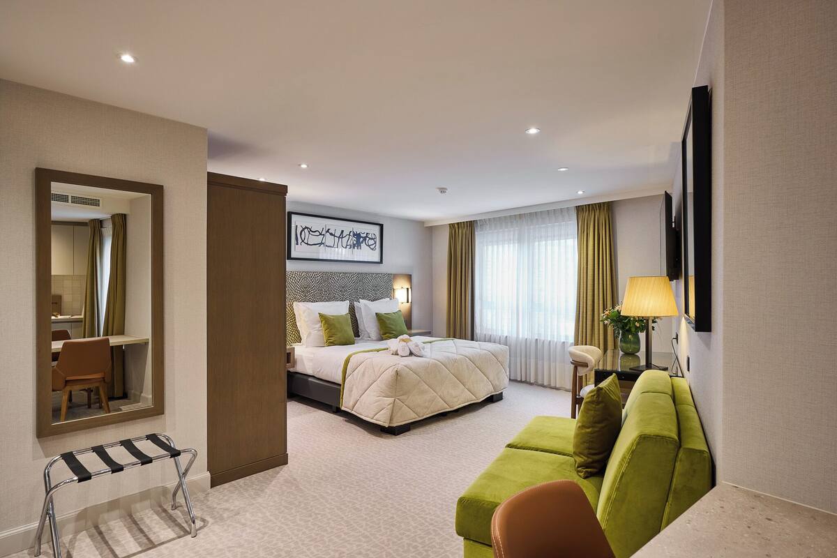 A hotel room with a bed, a green sofa, a desk, and a mirror.