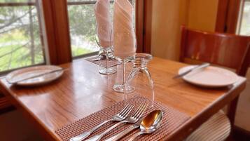A dining table set with clear glassware, silverware, and plates, with a view of trees through the window.