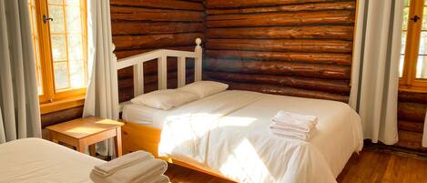 Un dormitorio de estilo cabaña de troncos con una cama individual, una mesita de noche pequeña y una ventana con cortinas.