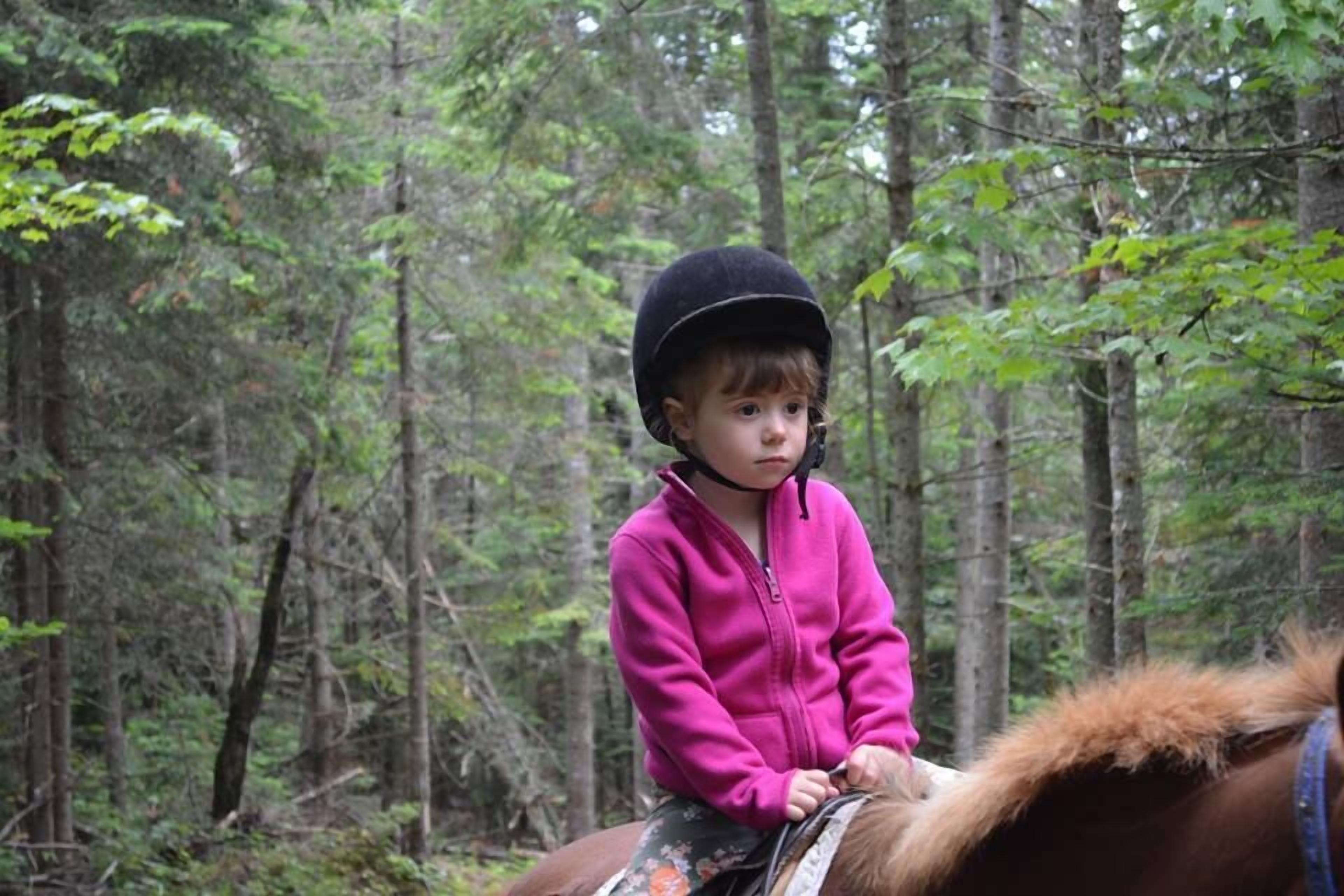 A child riding a horse in a forested area.