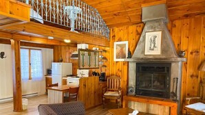 Interior acogedor de una cabaña con comedor de madera, sofá, chimenea y cocina con refrigerador y estufa.