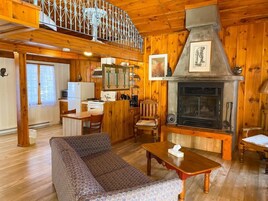 L’intérieur chaleureux d’un chalet comprend un coin repas en bois, un canapé, une cheminée et une cuisine équipée d’un réfrigérateur et d’une cuisinière.