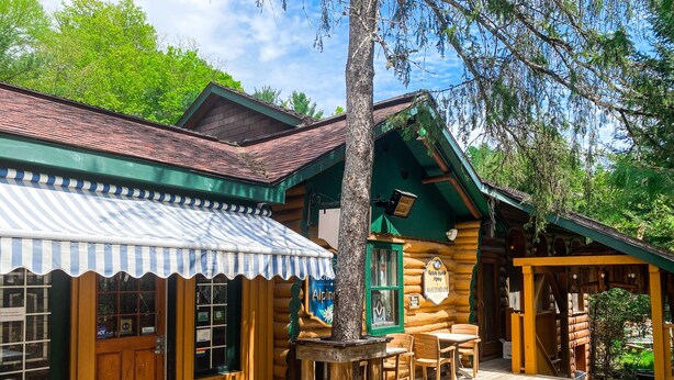 Un edificio rústico de madera con toldo a rayas, mesas al aire libre y un letrero que indica que es un restaurante.