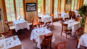 Un restaurante con varias mesas y sillas, amplias ventanas y un cuadro en la pared.