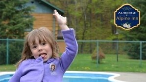 Niño con una chaqueta morada junto a una piscina, con un cartel de Auberge Alpine Inn al fondo.