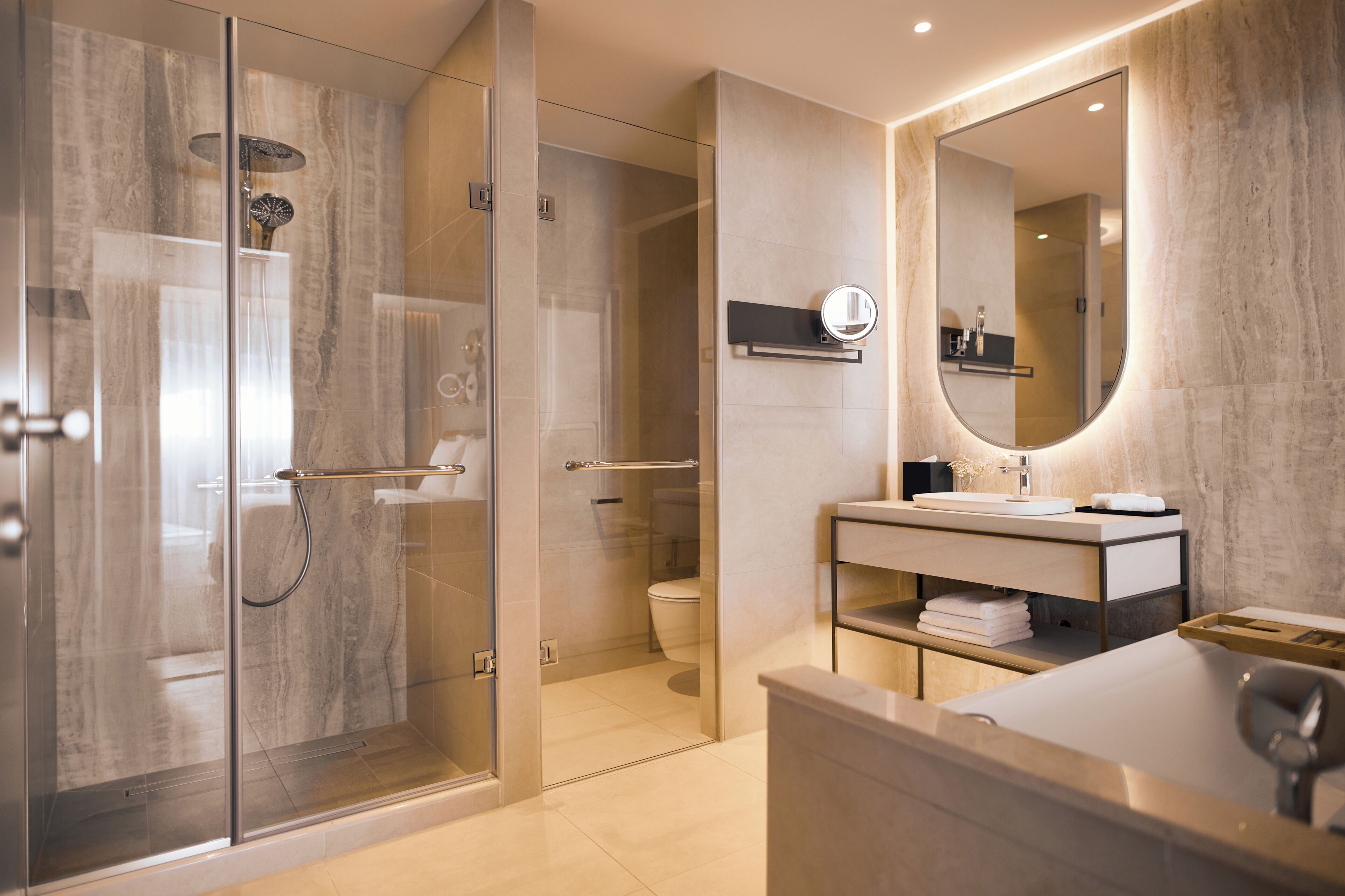 A modern bathroom with a glass-enclosed shower, a large mirror, and a vanity with a sink and towel storage.