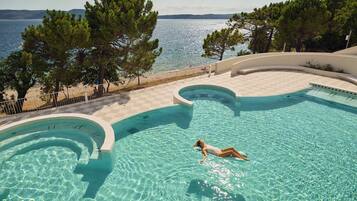 Una piscina con una persona flotando, rodeada de árboles y vista al mar.
