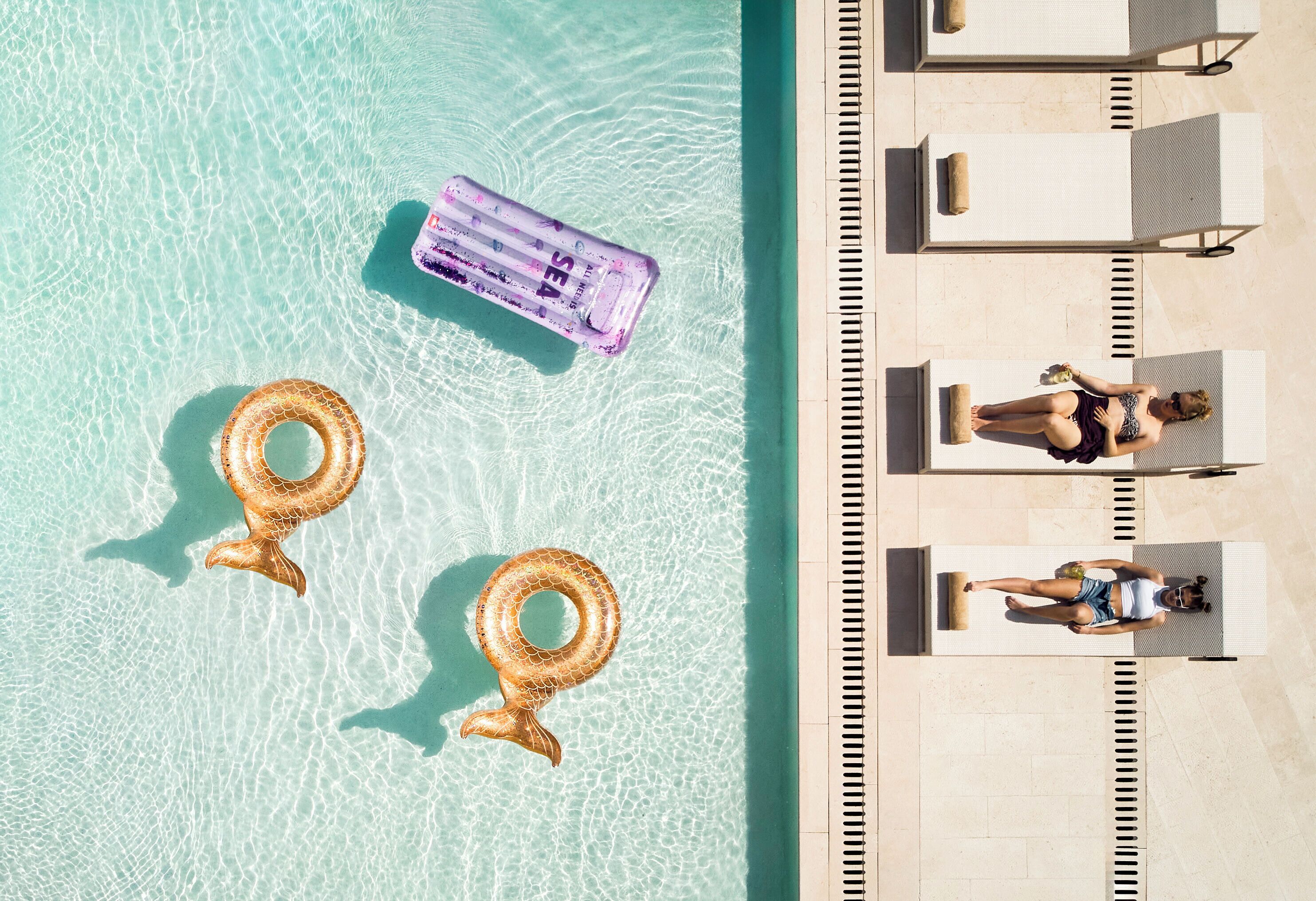 Vue aérienne d’une piscine avec deux bouées en forme de sirène et une bouée violette.
