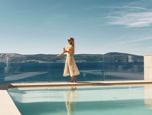 Una mujer con un vestido parada junto a una piscina con vistas al mar y colinas.