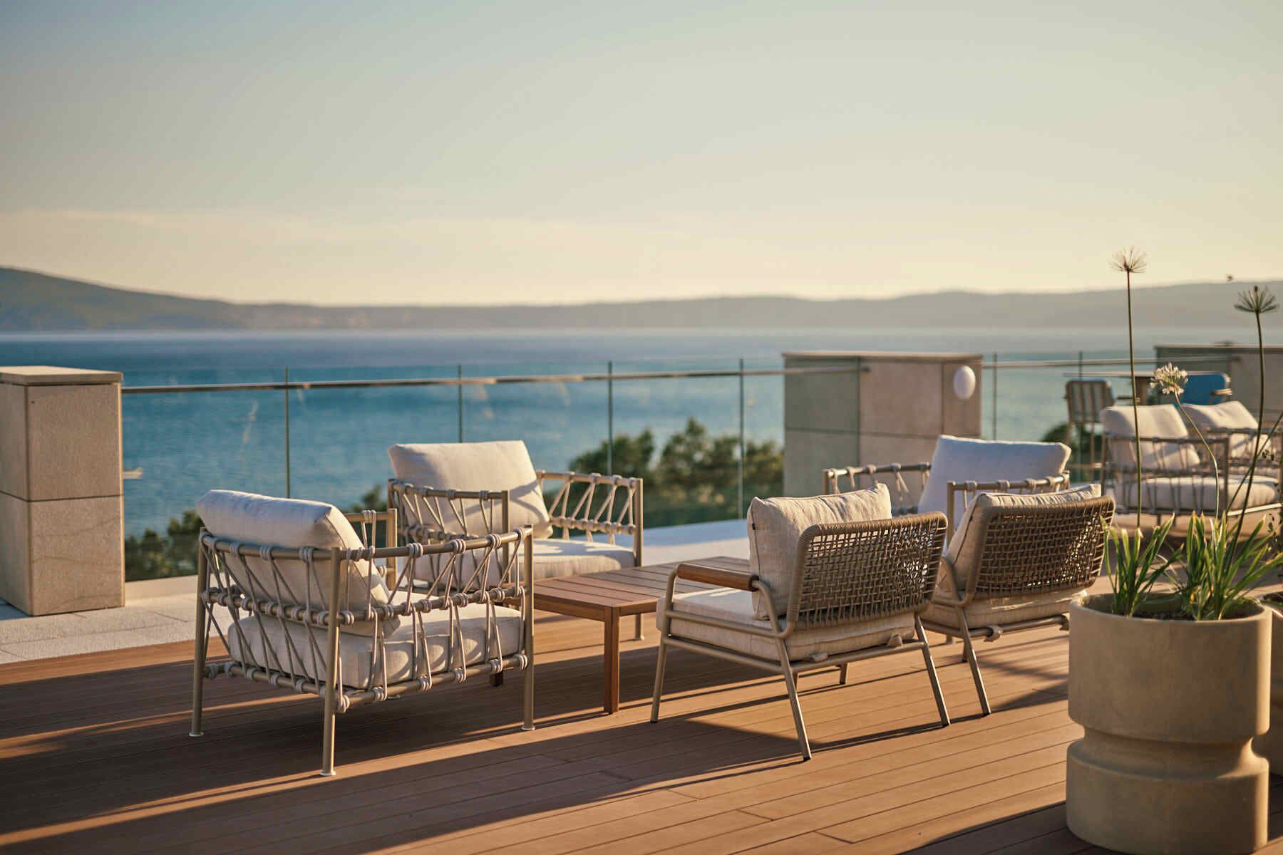 Terraza con sillas de mimbre y una mesa, con vista a un cuerpo de agua.