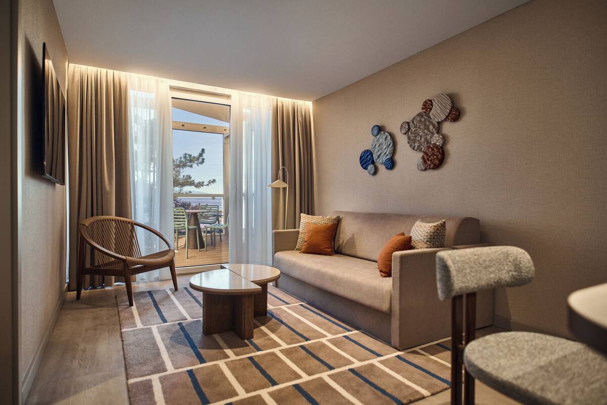 Una sala de estar moderna con un sofá, un sillón, una mesa de centro y vistas al exterior a través de un ventanal.