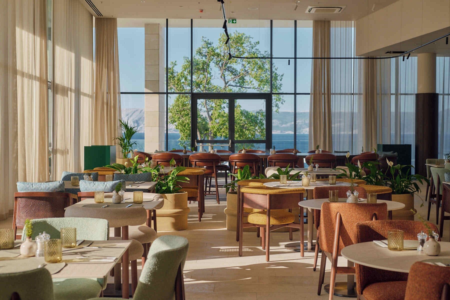 Un comedor amplio con varias mesas y sillas, ventanas grandes con vistas al exterior y una decoración interior moderna.
