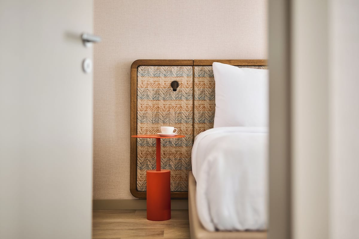 Una habitación de hotel con cama, una mesita con una taza y un cabecero estampado.