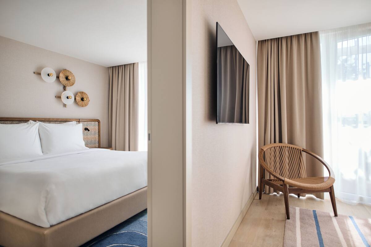 Una habitación de hotel con cama, sillón, televisor y cortinas.