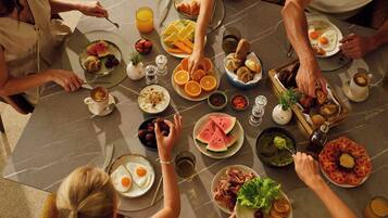 A group of people dining at a marble table with various dishes, including eggs, fruits, and bread.