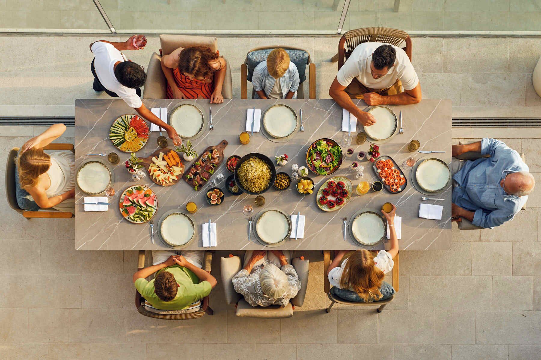 Un groupe de personnes est assis autour d’une grande table à manger, devant divers plats et boissons.