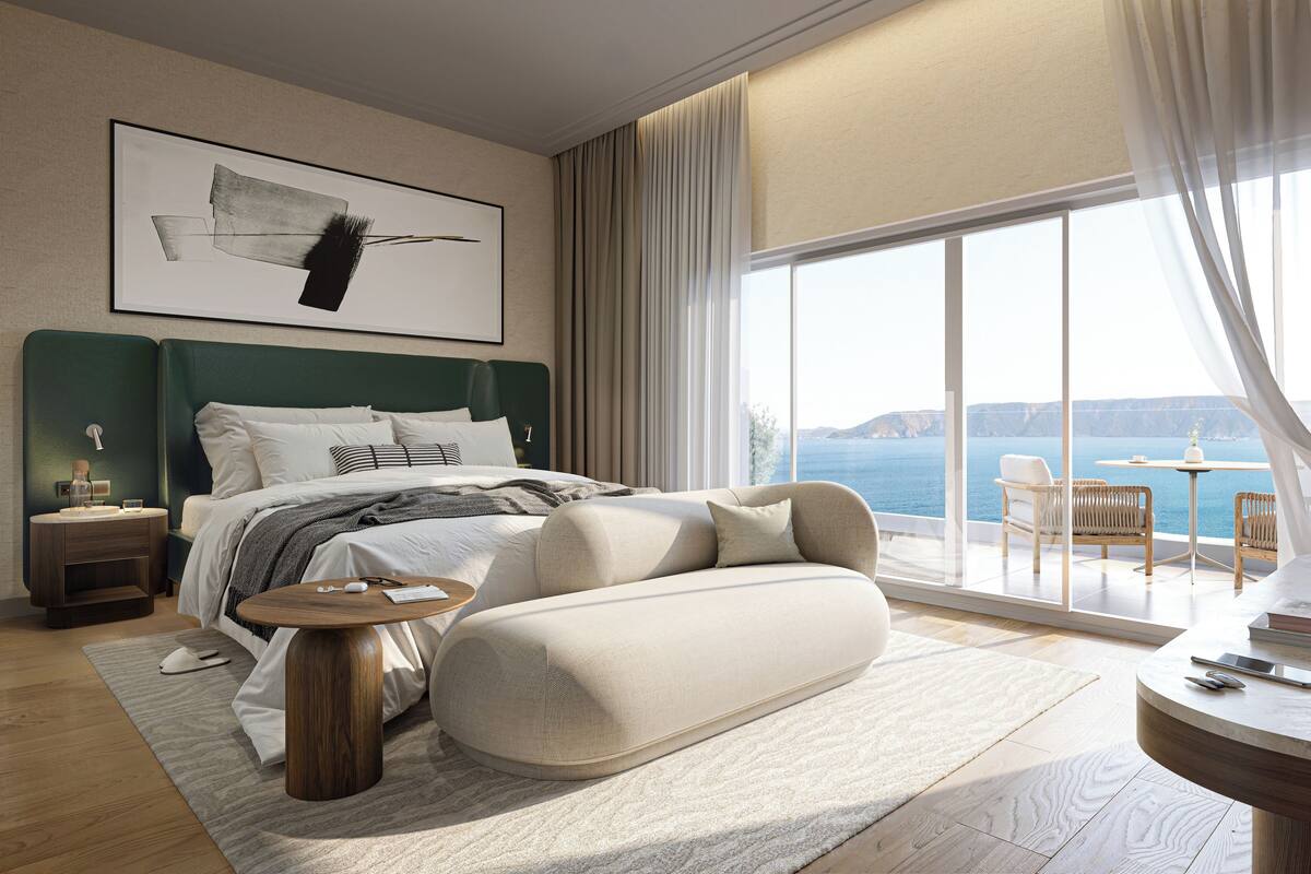 Un dormitorio moderno con una cama grande, una mesita de noche, una mesa redonda de centro y vistas al mar.