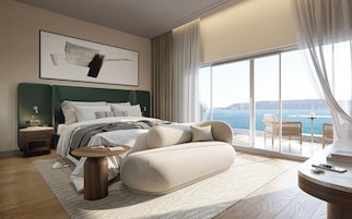A modern bedroom with a large bed, a side table, a round coffee table, and a view of the sea.