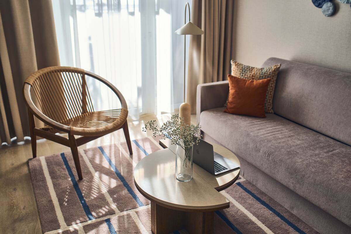 Una habitación con un sofá, una silla, una mesita con un ordenador portátil y un jarrón de flores.