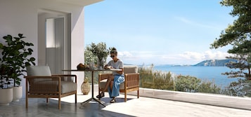 A modern outdoor seating area with a view of the sea, featuring wicker furniture and a table with a vase of flowers.
