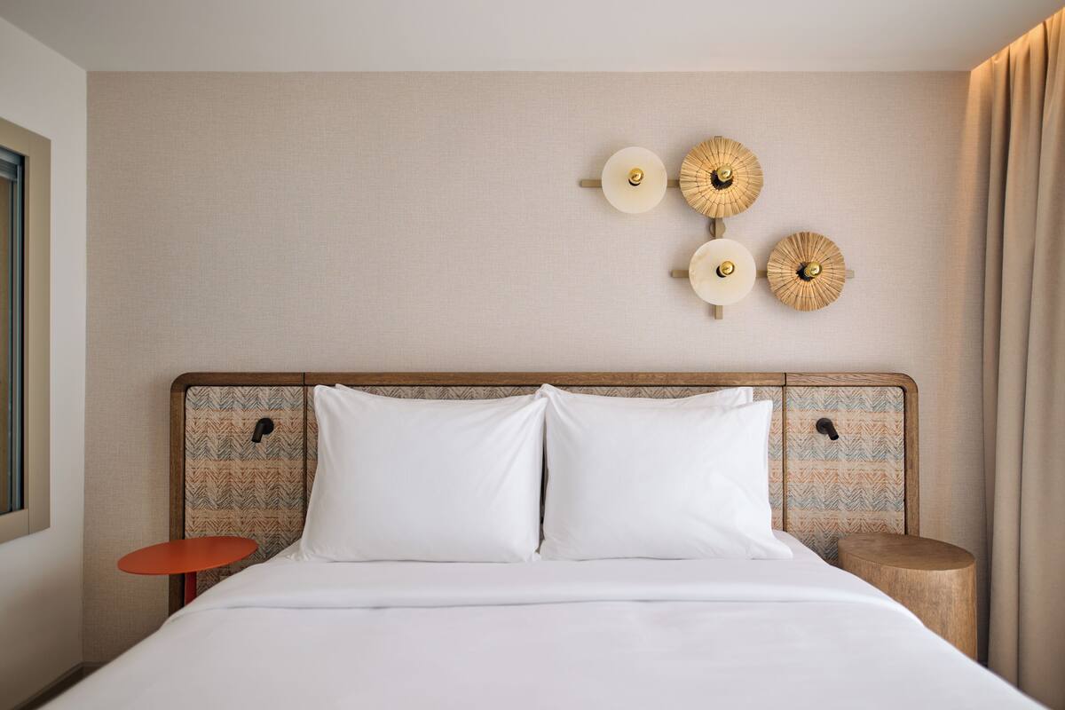 Una habitación de hotel con una cama, una mesita, una mesita de noche y lámparas de pared.