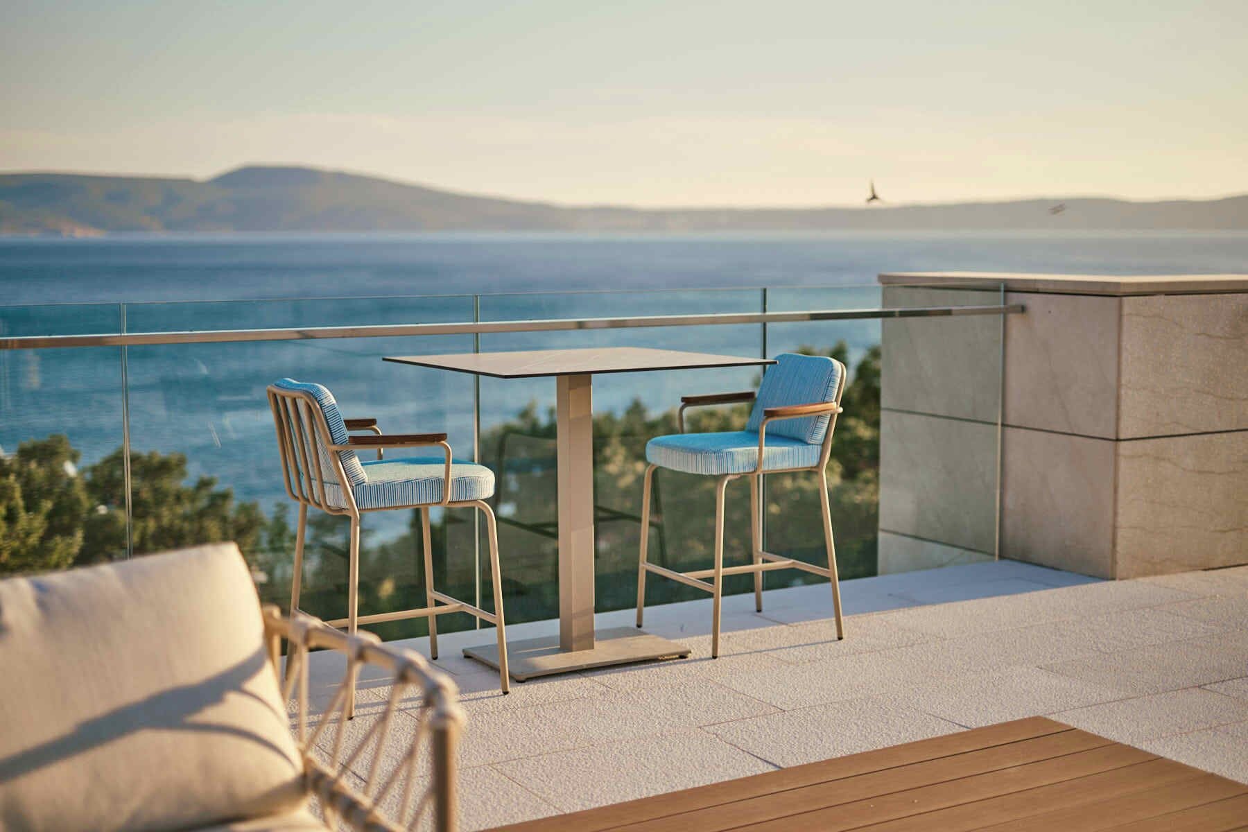 A balcony with a table and two chairs, overlooking a body of water and distant land.