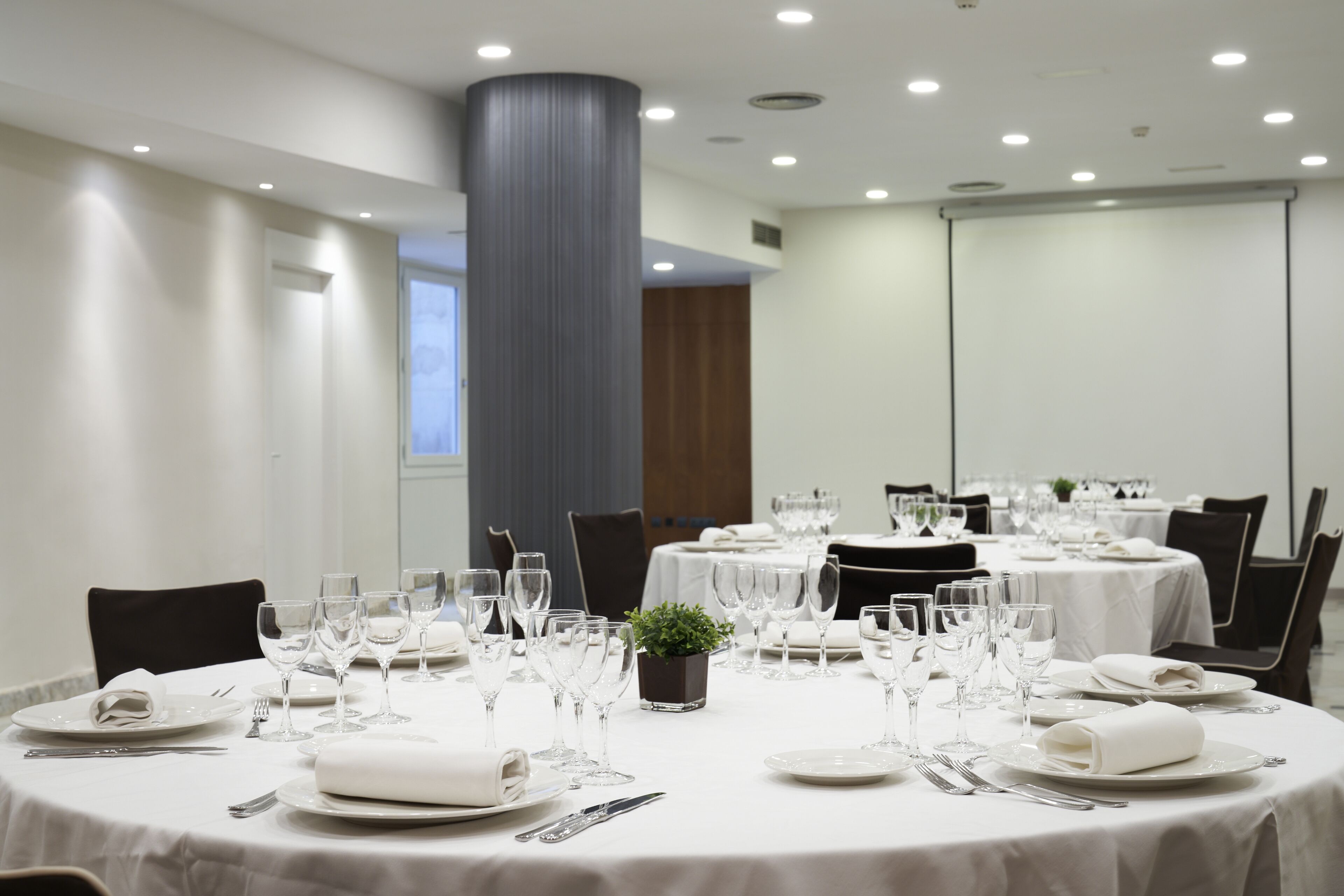 A conference room with round tables set for a meeting, equipped with chairs, plates, cutlery, and glassware.