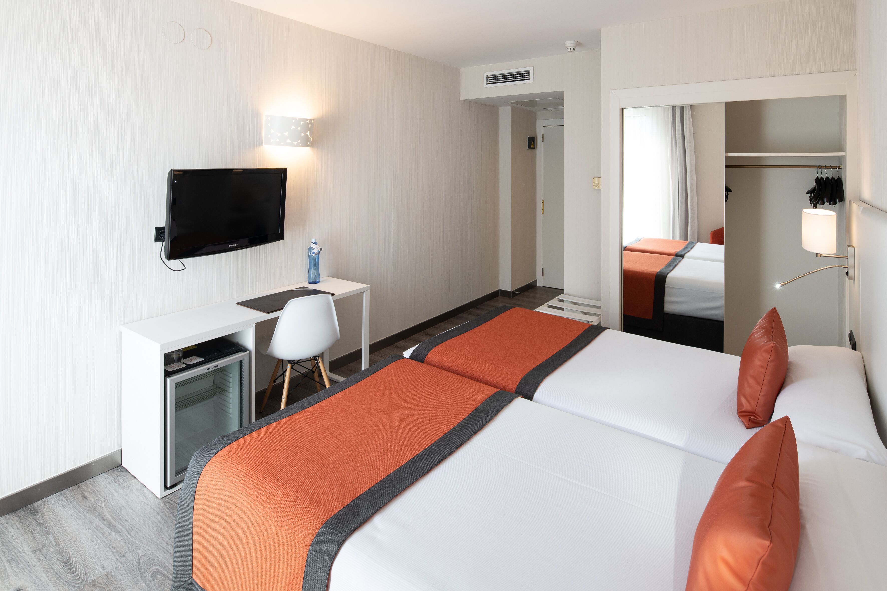 Une chambre d’hôtel comprenant un lit, un bureau avec un ordinateur, une télévision et une armoire.