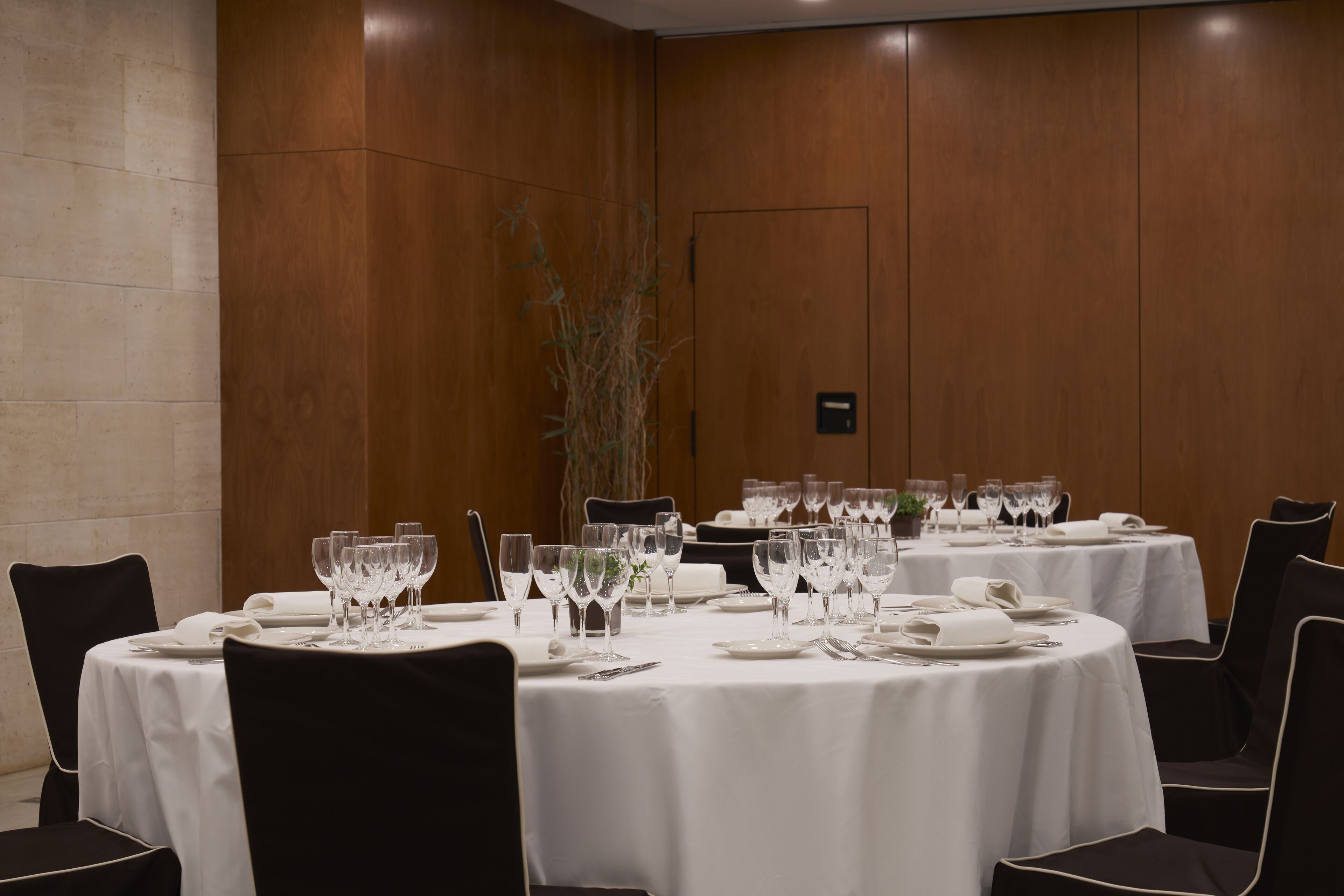 Una sala conferenze con tavoli rotondi apparecchiati per una riunione, completa di sedie, piatti, posate e bicchieri.