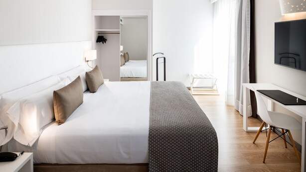 Une chambre d’hôtel moderne avec un lit bien fait, un bureau avec une chaise, un téléviseur à écran plat et une armoire.