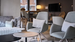 Un espace de détente moderne avec des fauteuils à revêtement gris, une table ronde et un canapé agrémenté de coussins à carreaux.