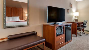 A hotel room with a bed, a TV, a desk with a chair, a lamp, and a large mirror.