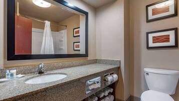 A bathroom with a granite sink, a mirror, a toilet, and framed pictures on the wall.