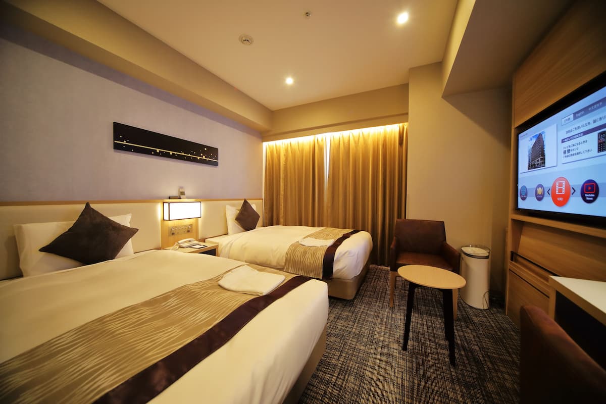 A hotel room with two beds, a desk, a chair, a TV, and a curtain.