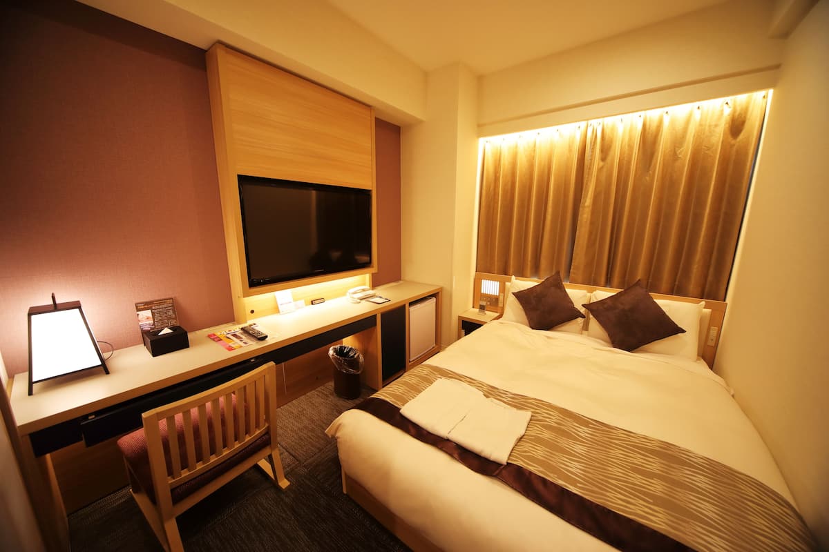 A hotel room with a bed, desk, and TV.