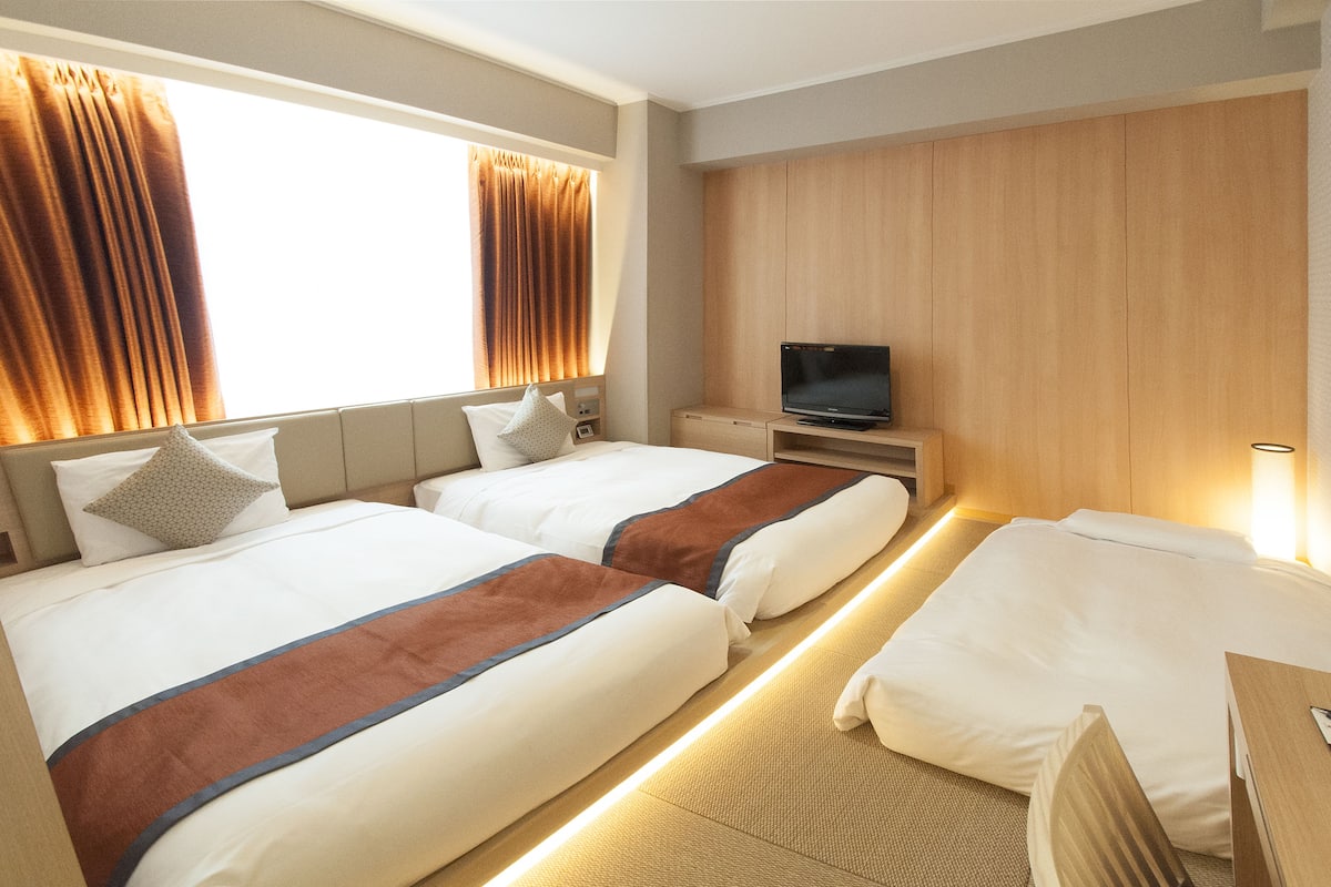 A hotel room with two beds, a TV, and a wooden wardrobe.