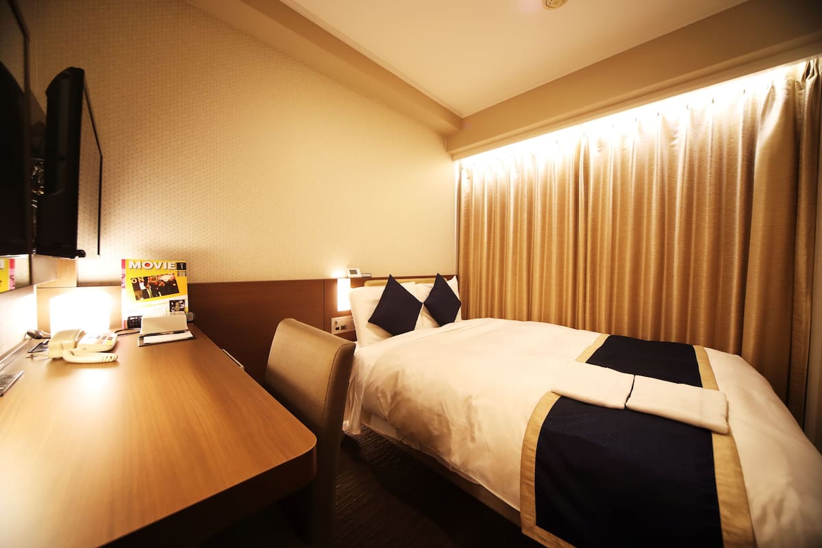 A hotel room with a bed, a desk with a telephone, and a magazine on the nightstand.