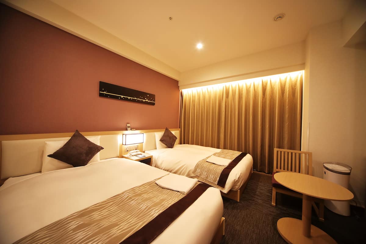 A hotel room with two beds, a desk, a chair, a lamp, and a curtain.