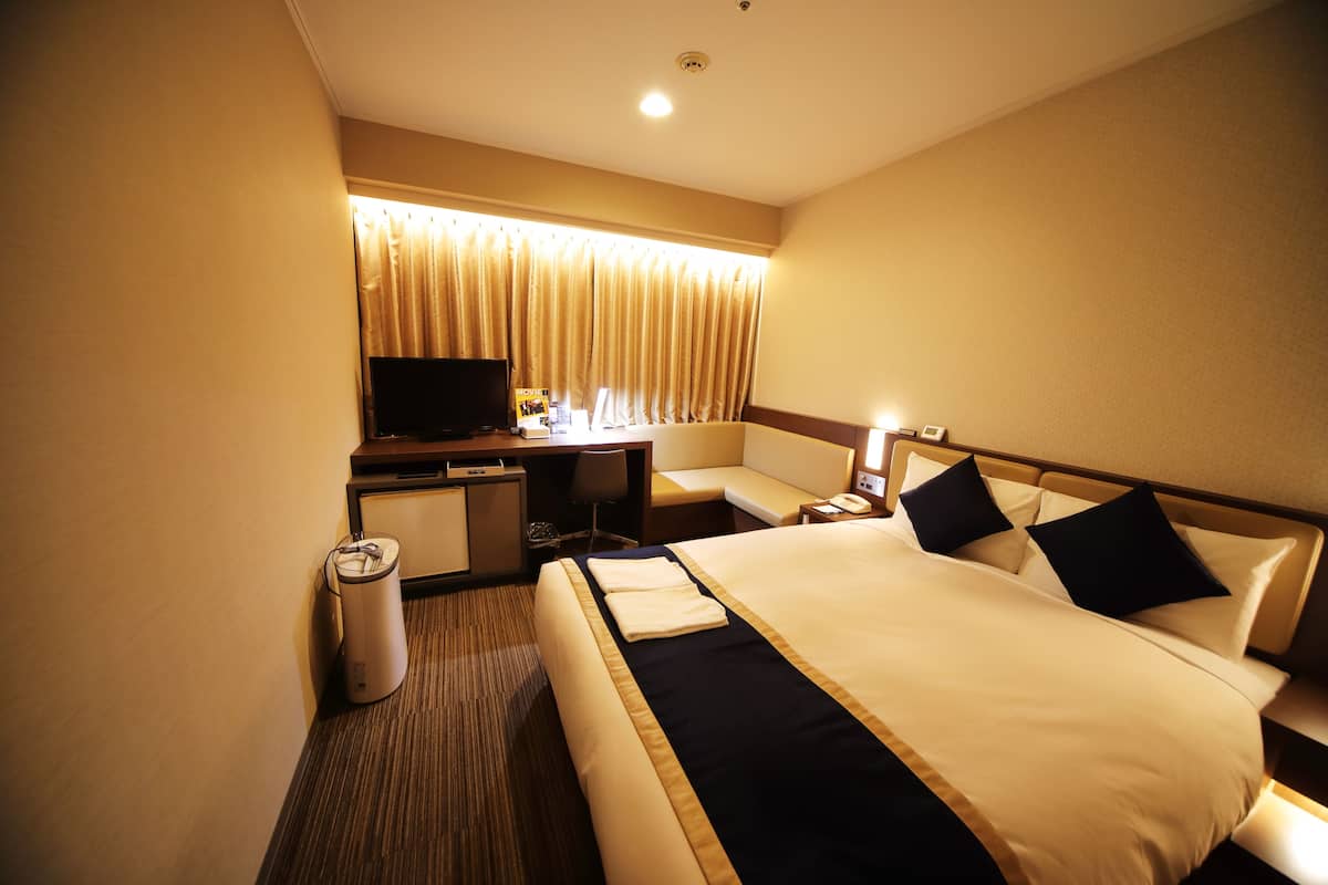 A hotel room with a bed, a desk, a television, and a window with curtains.